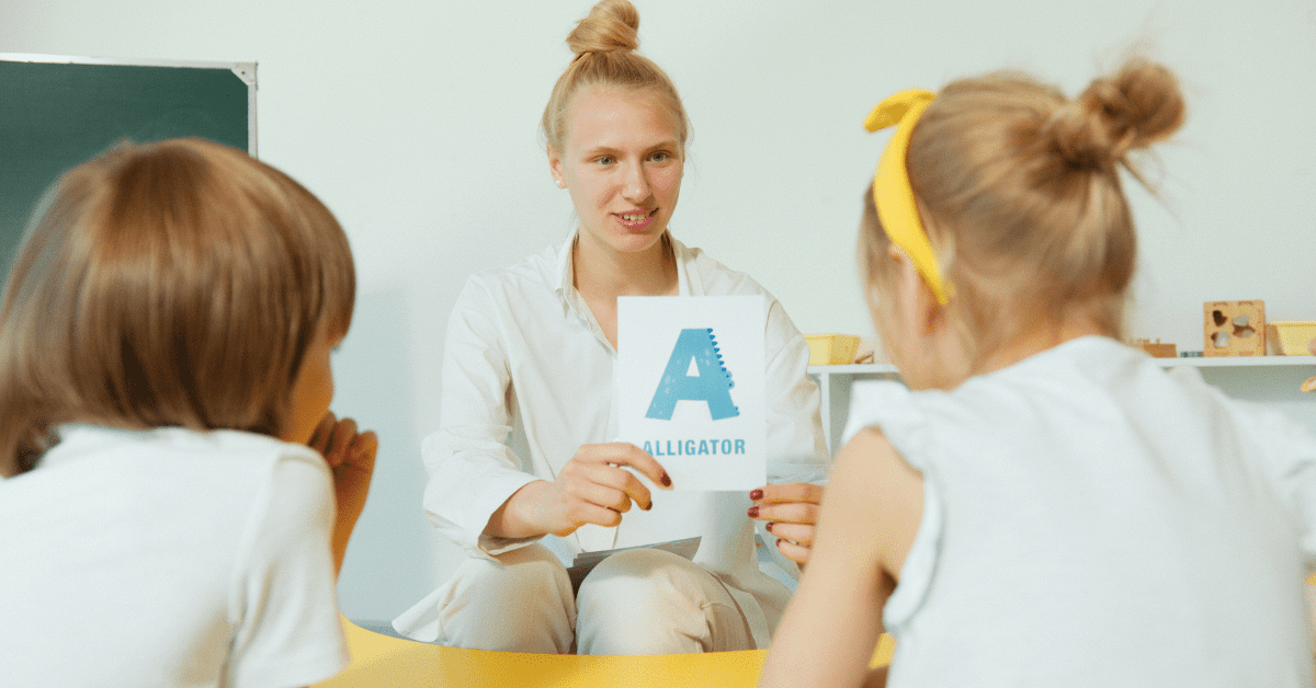 Preschool teacher showing a big A letter to two students