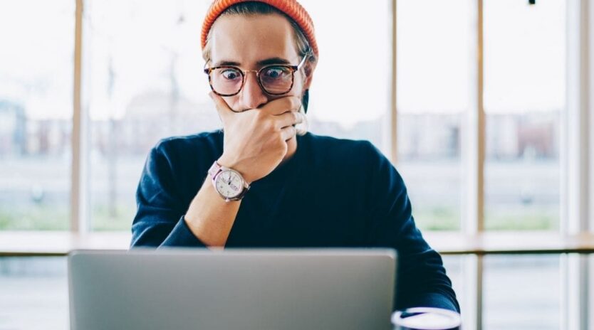 Shocked young hipster guy in spectacles amazed with 4G connection watching webinar online on netbook, surprised caucasian male shocked with received email about web store sales on laptop computer