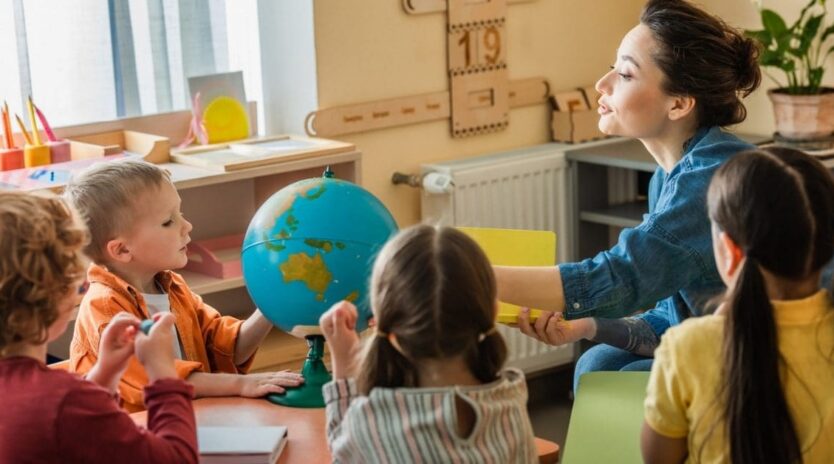 Young teacher talking to children near globe during lesson
